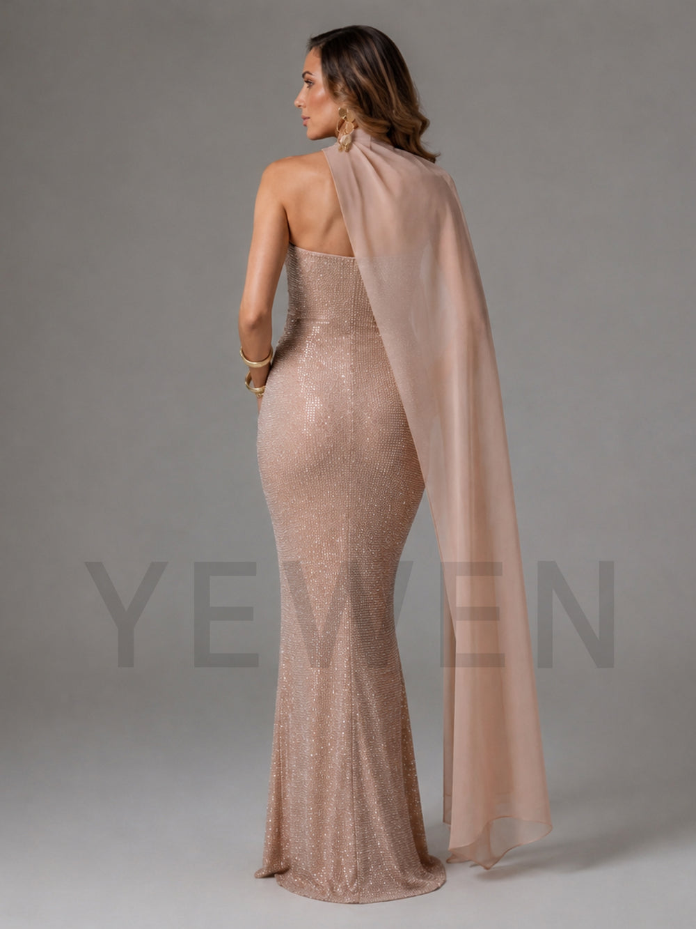 A woman modeling a floor-length, strapless champagne beige sequined gown with a matching sheer draped cape, shown from the back against a neutral gray studio background.