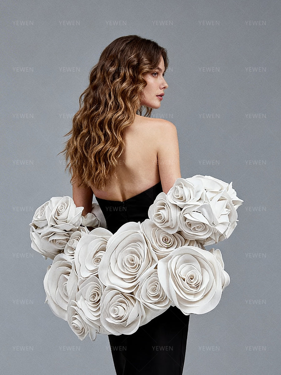 Close-up back view of a model wearing a black elegant evening dress highlighting the detachable 3D white floral cape and zipper back.