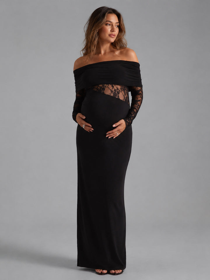 A pregnant woman modeling a black off-the-shoulder maternity maxi dress with long sheer lace sleeves and a lace panel at the waist, photographed against a solid gray studio background.