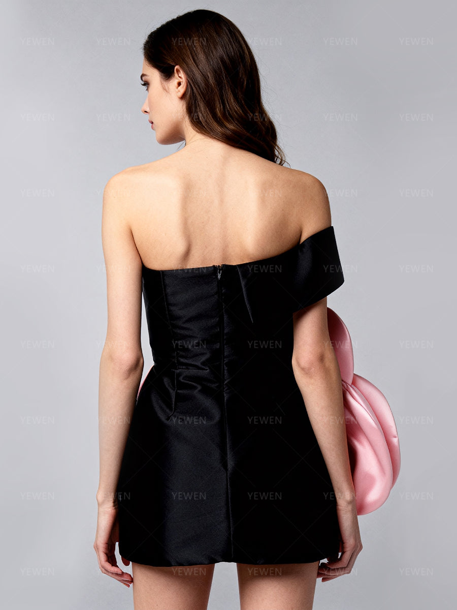 Back view of a model wearing a black satin off-shoulder mini dress with a pink 3D oversized floral applique for party gown.