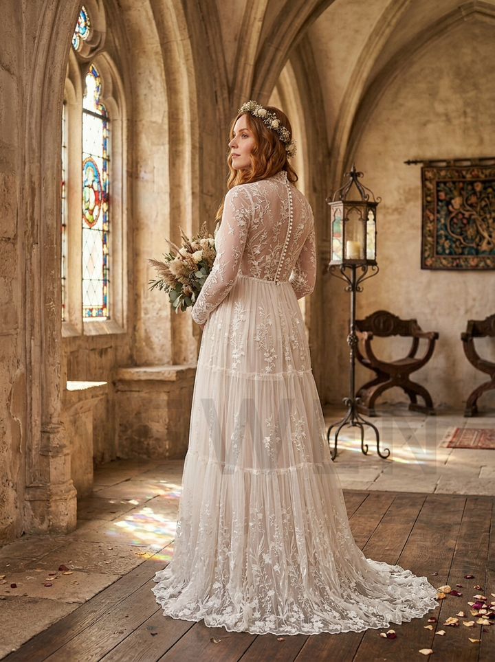 A bride in a long-sleeve lace wedding gown stands with her back to the camera inside a stone church or chapel, holding a bouquet of dried flowers. The scene features warm, golden light from stained glass windows, wooden floors, and rustic interior details.