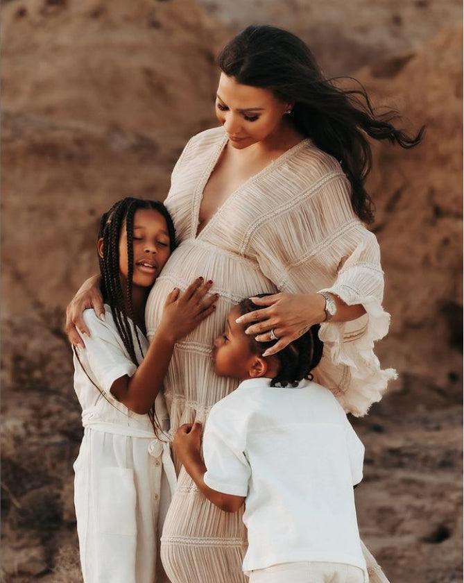 Woman in a beige dress surrounded by two children in a desert setting