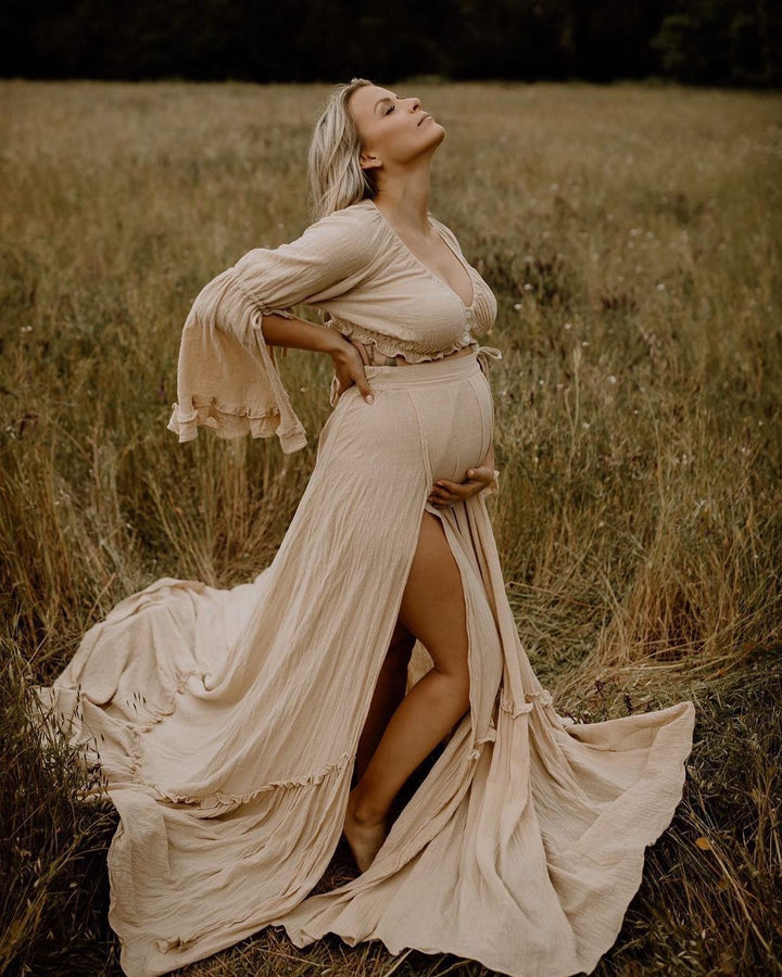 Pregnant woman in a flowing beige dress standing in a field.
