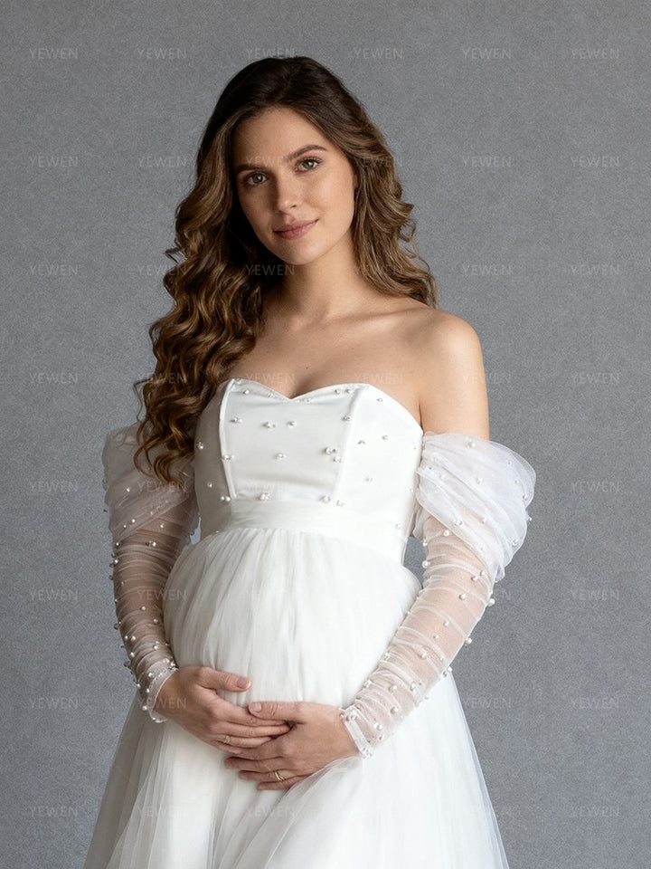 Close-up front view of a pregnant model wearing a custom maternity wedding dress highlighting the sweetheart neckline and pearl sleeves.