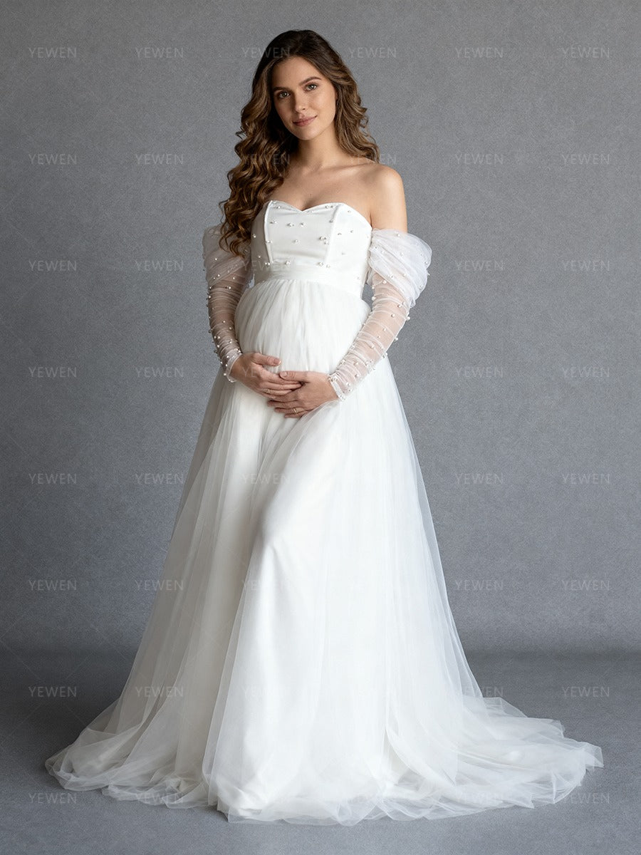 Front view of a pregnant model wearing a custom maternity wedding dress with pearl sleeves and flowing tulle skirt.