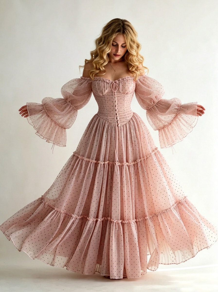 A woman modeling a dusty pink off-the-shoulder maxi dress with a tiered ruffled skirt and voluminous bell sleeves, set against a plain light background.