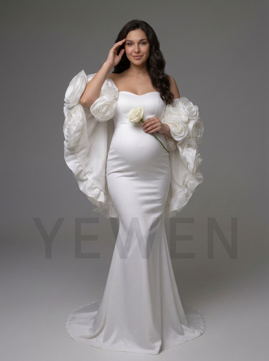 A pregnant model wearing a white strapless mermaid gown with dramatic oversized floral ruffle sleeves, holding a white rose against a neutral gray studio background. A faint 'YEWEN' watermark is visible across the lower portion.
