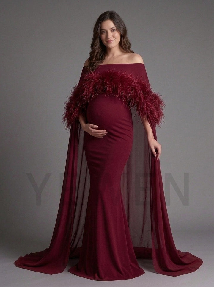 Side profile of a burgundy maternity baby shower gown with a feather-trimmed cape.