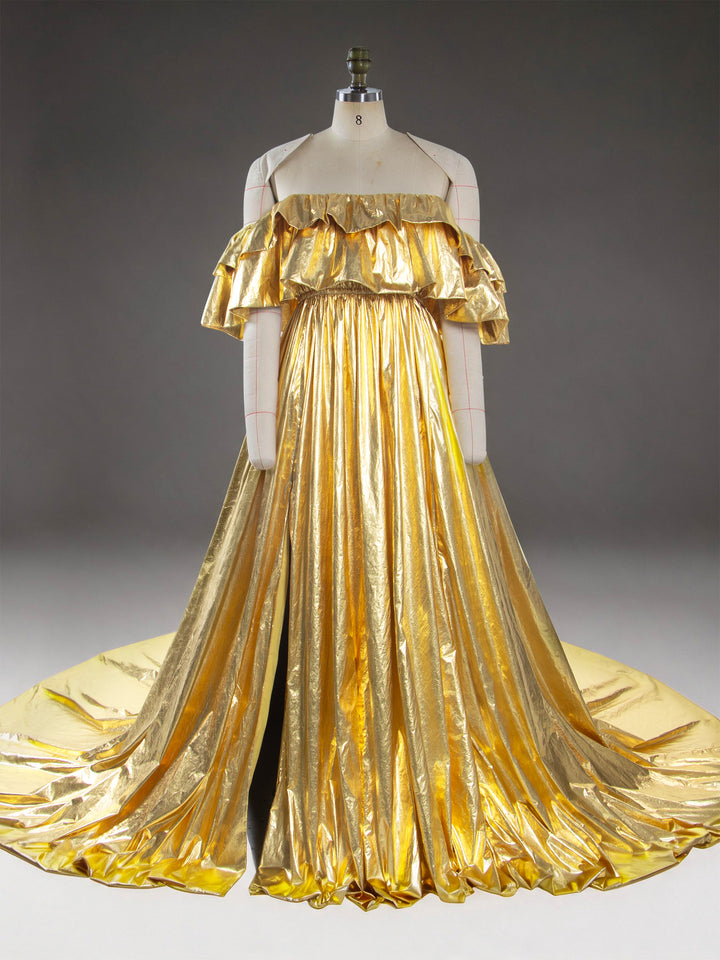 A metallic gold off-the-shoulder gown displayed on a cream dress form mannequin against a dark gray studio background.