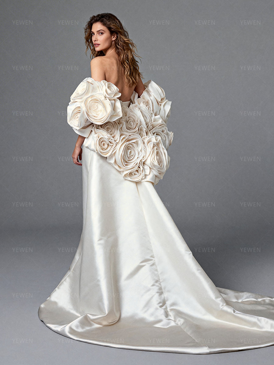Back view of a model wearing an ivory satin off-shoulder mermaid wedding dress with a 3D floral cape.