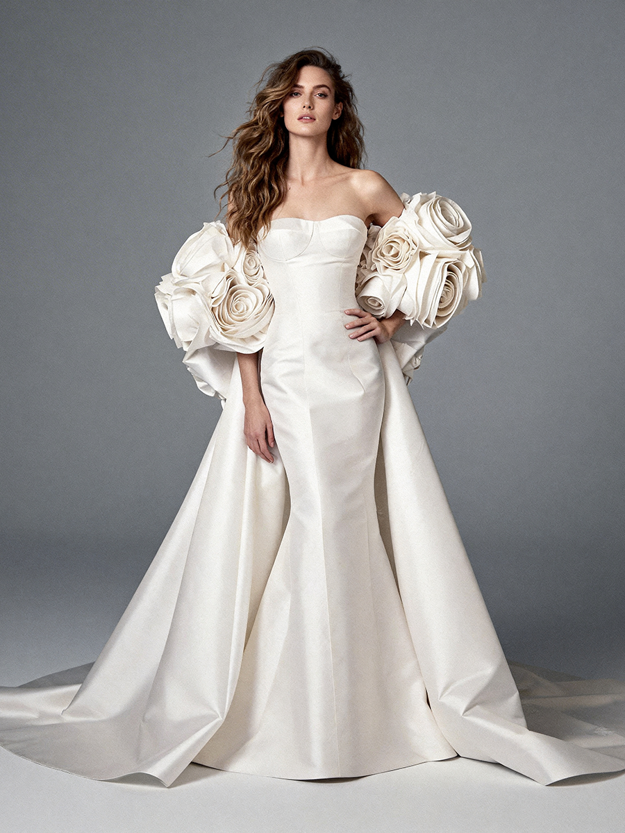 Full front view of a model wearing an ivory satin off-shoulder mermaid wedding dress with a 3D floral cape.