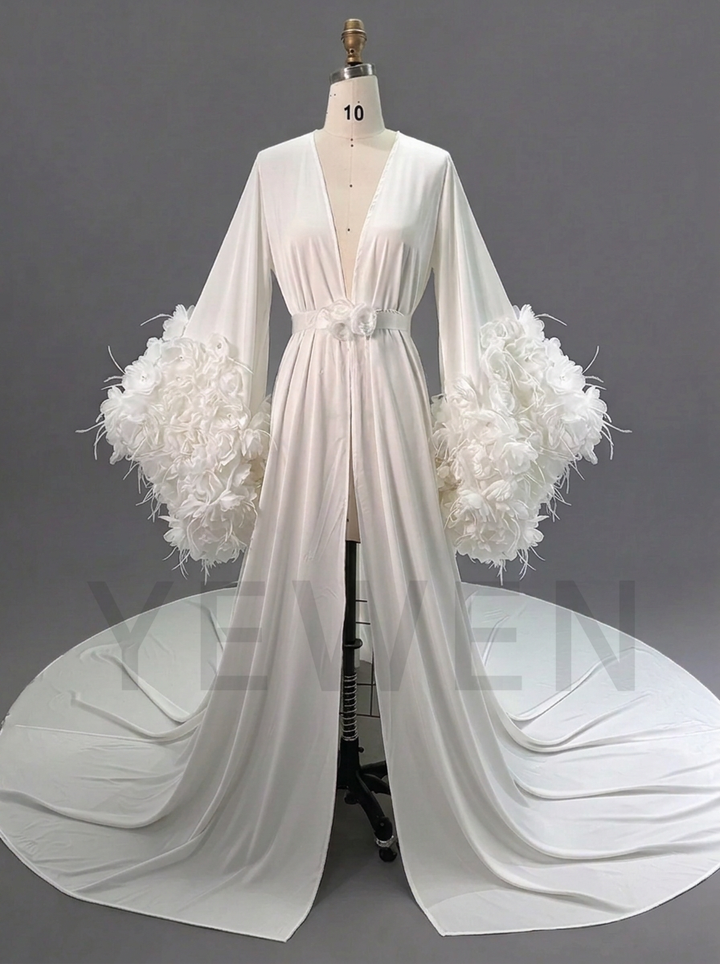 A long white kimono-style gown displayed on a mannequin against a gray studio background. The dress has a deep V-neckline, a matching waist belt, and dramatic feathered balloon sleeves with a long train extending across the floor.