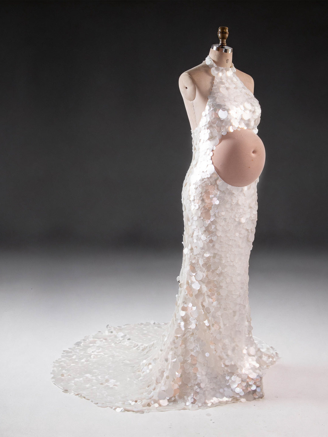 Side profile of an ivory sequin maternity baby shower gown with a halter neck and cutout belly.
