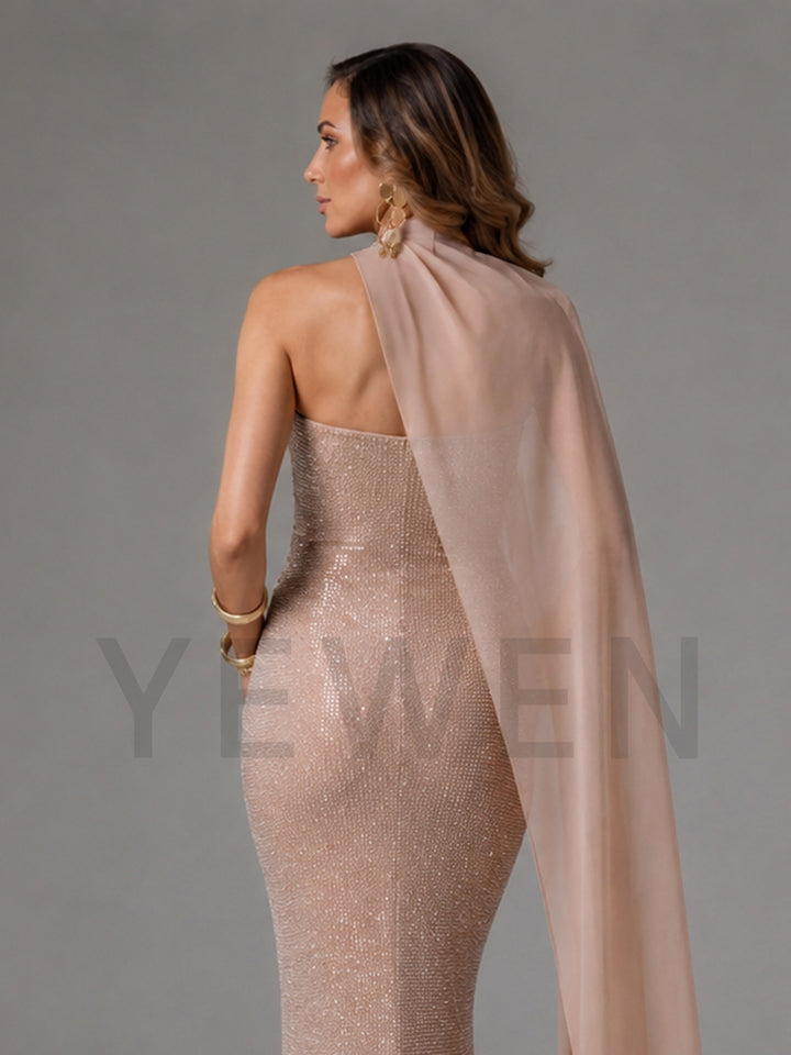 A woman shown from the back wearing a fitted champagne-beige sequined gown with a sheer matching draped scarf, against a plain gray studio background.