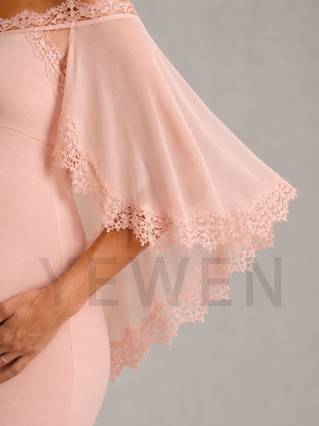 A close-up of a model wearing a light pink dress with a sheer flutter sleeve featuring intricate floral lace trim, set against a solid gray background.
