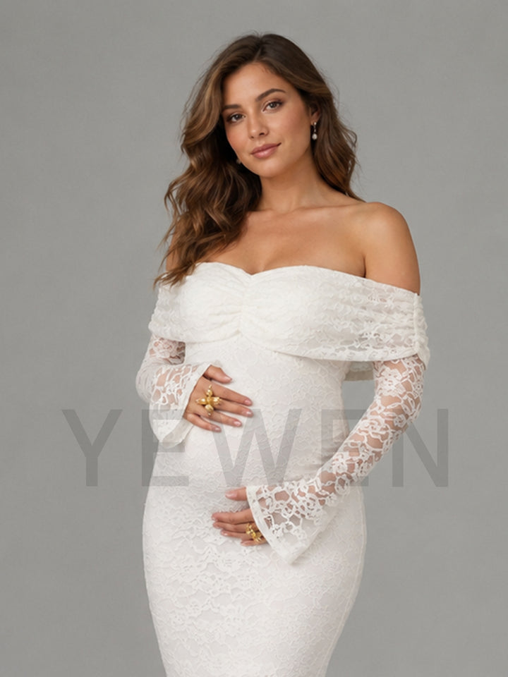 A pregnant woman wearing an off-the-shoulder white lace maternity gown with long lace sleeves, standing against a solid gray studio background.