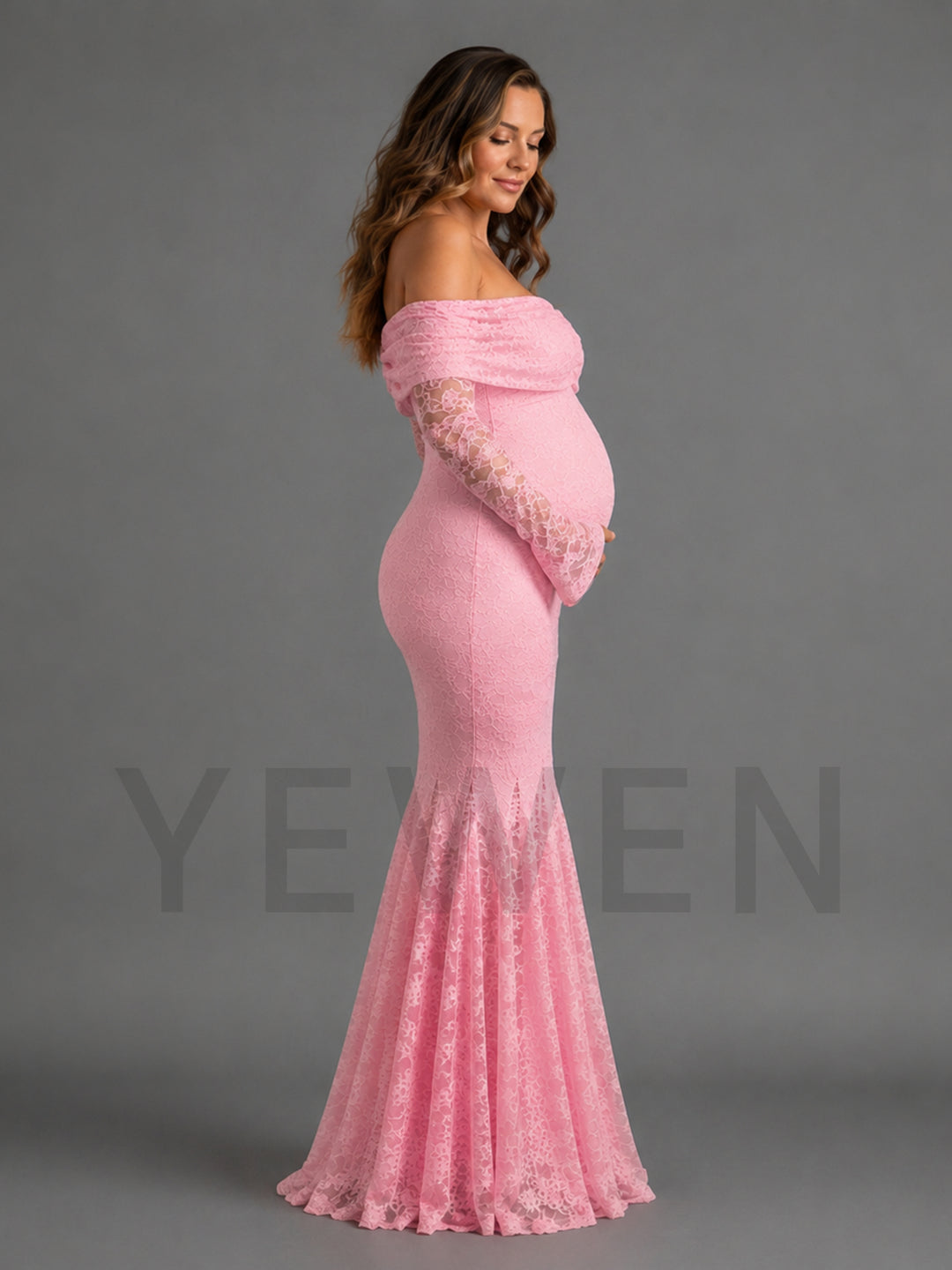 A pregnant model wearing a pink off-the-shoulder maternity gown with long lace sleeves and a flared lace hem, photographed against a plain gray studio background.