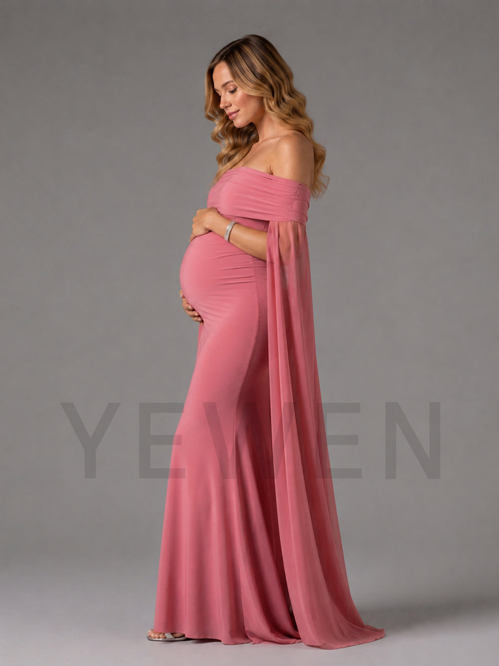 A pregnant woman wearing a dusty pink off-the-shoulder maternity gown with a flowing cape-like overlay, standing in profile against a solid gray studio background. A faint 'YEWEN' brand watermark is visible across the lower portion of the image.