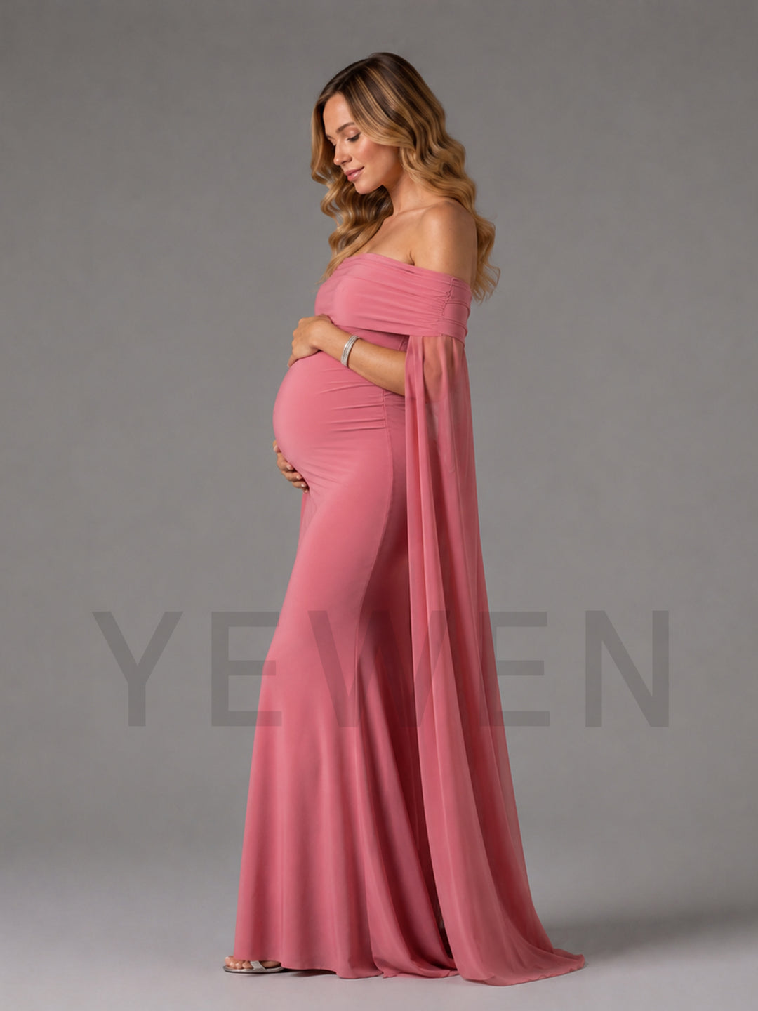 A pregnant woman wearing a dusty pink off-the-shoulder maternity gown with a flowing cape-like overlay, standing in profile against a solid gray studio background. A faint 'YEWEN' brand watermark is visible across the lower portion of the image.