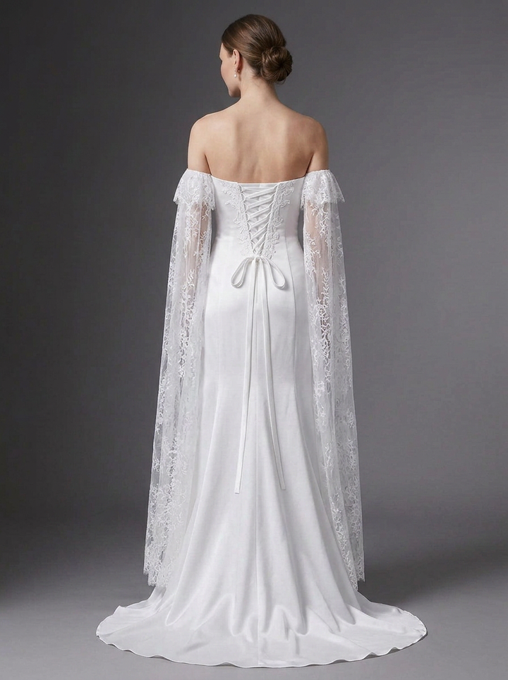 A woman shown from the back wearing an off-the-shoulder white wedding gown with a lace corset back and long sheer lace cape sleeves, photographed against a dark gray studio background.