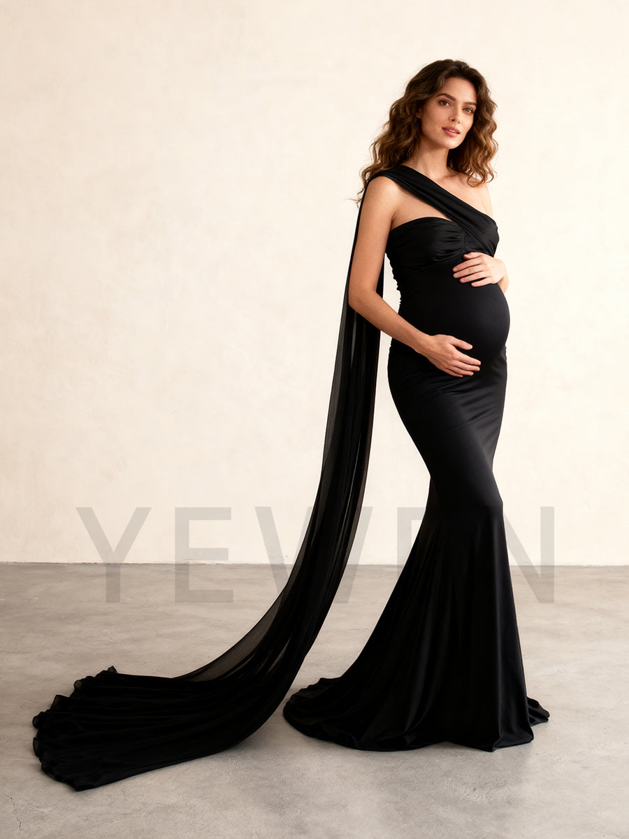 Woman wearing a black one-shoulder gown with a long train, standing against a plain background.