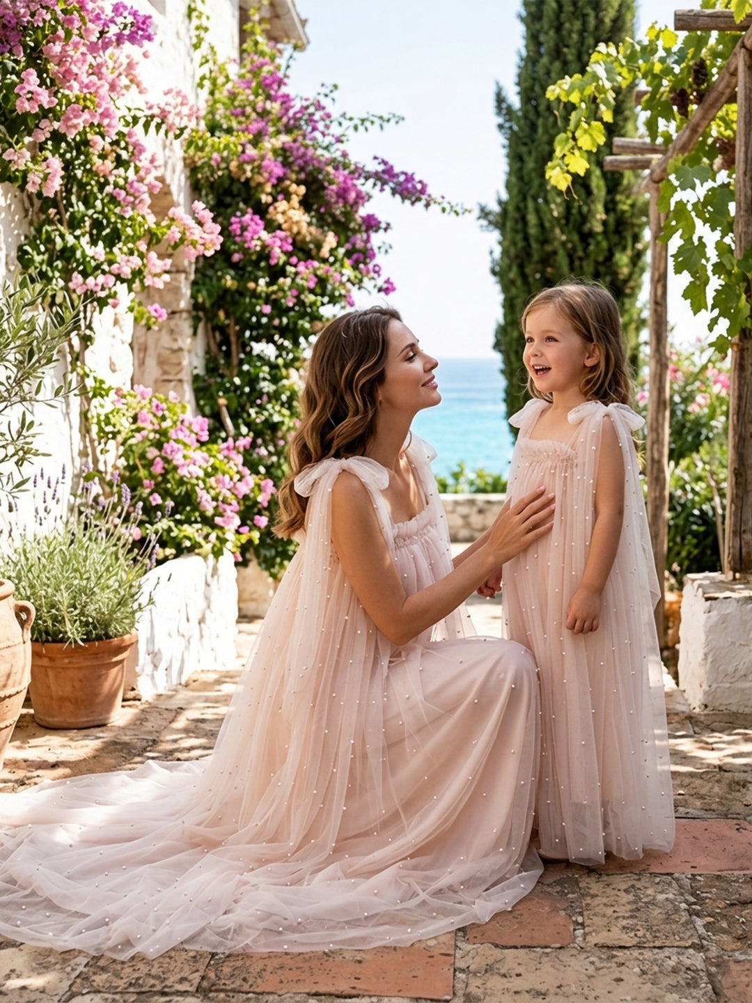 Blush pink sheer cape pearl tulle dresses for mommy and me, worn in an outdoor garden setting.