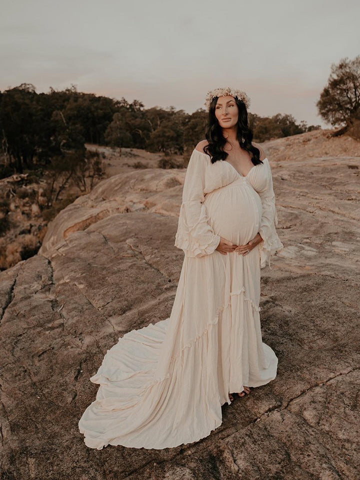 Woman in a flowing white dress standing on a rocky landscape with trees in the background