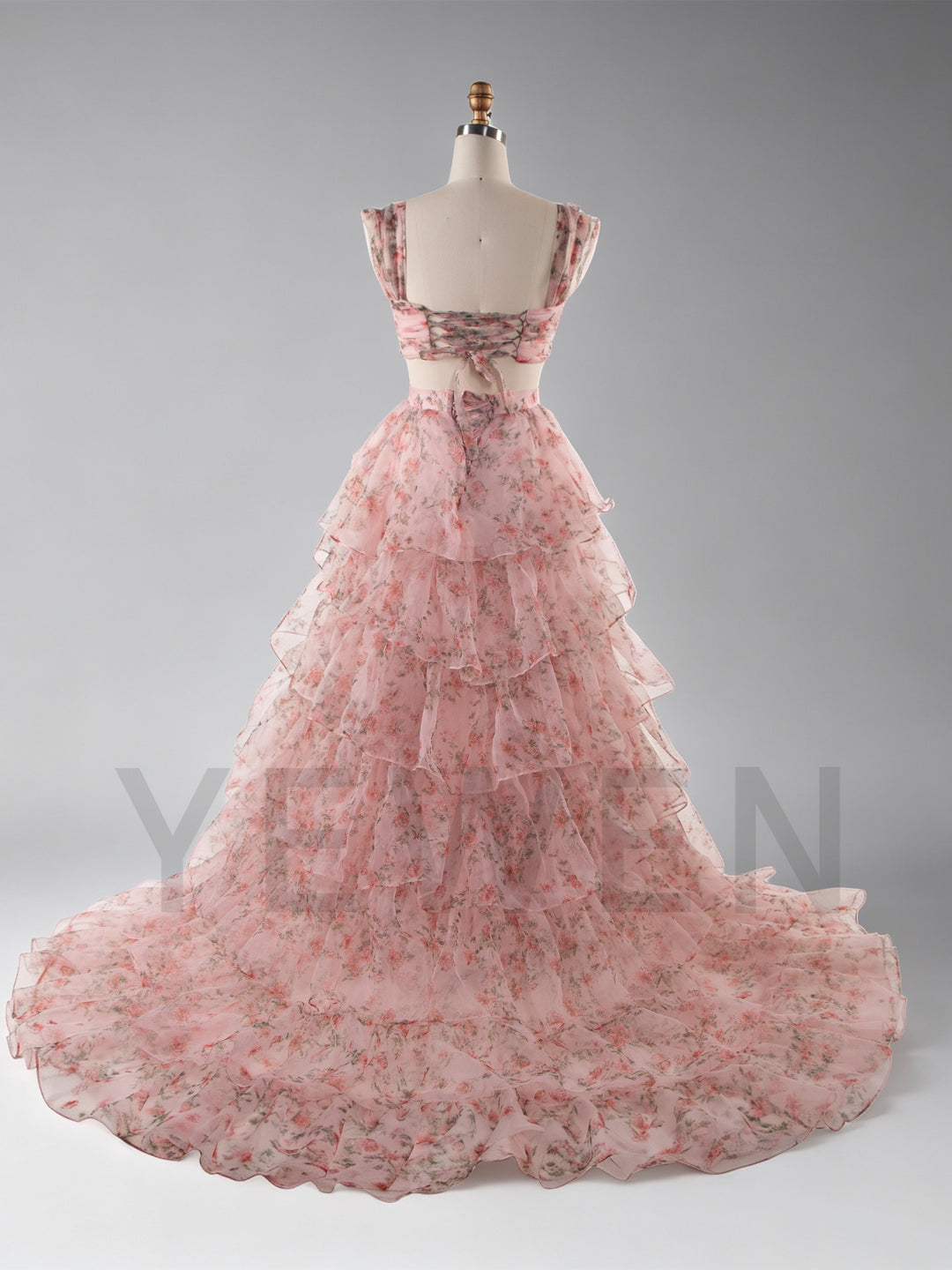 A pink tiered organza ball gown with a floral print, displayed on a mannequin against a gray studio background.
