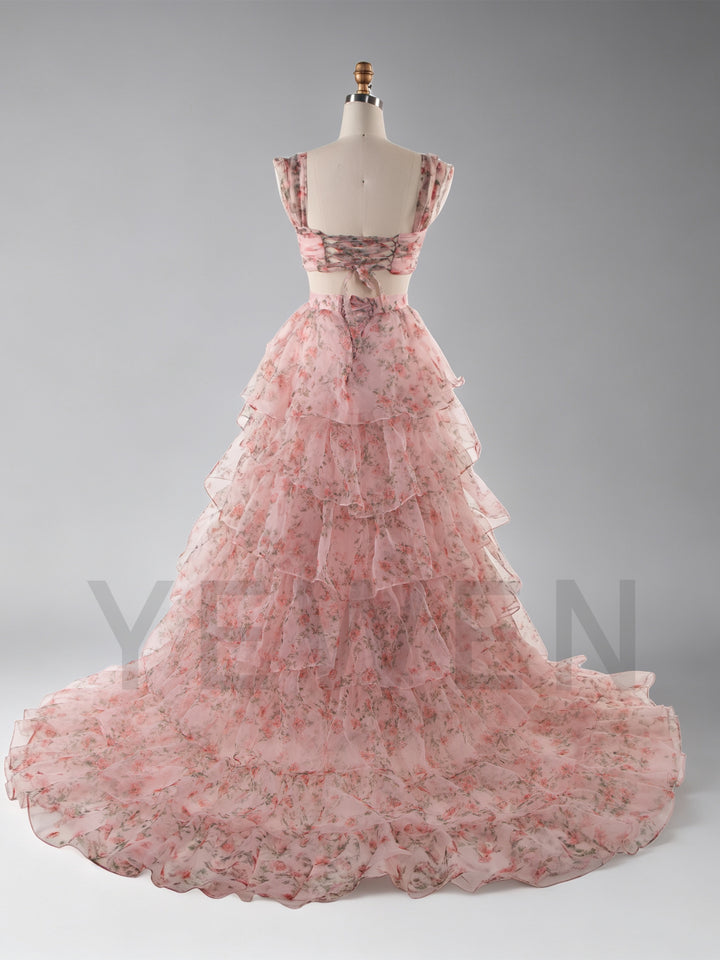 A pink tiered organza ball gown with a floral print, displayed on a mannequin against a gray studio background.