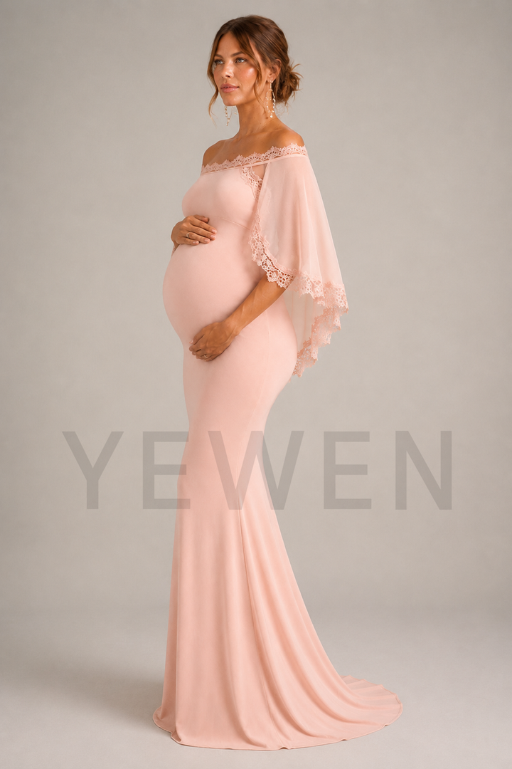 A pregnant woman modeling a light pink off-the-shoulder maternity gown with lace trim and a flowing train against a neutral gray studio background.