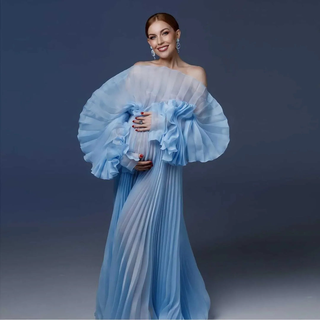 A pregnant woman wearing a white, pleated, organza maternity dress with long sleeves for a photo shoot.