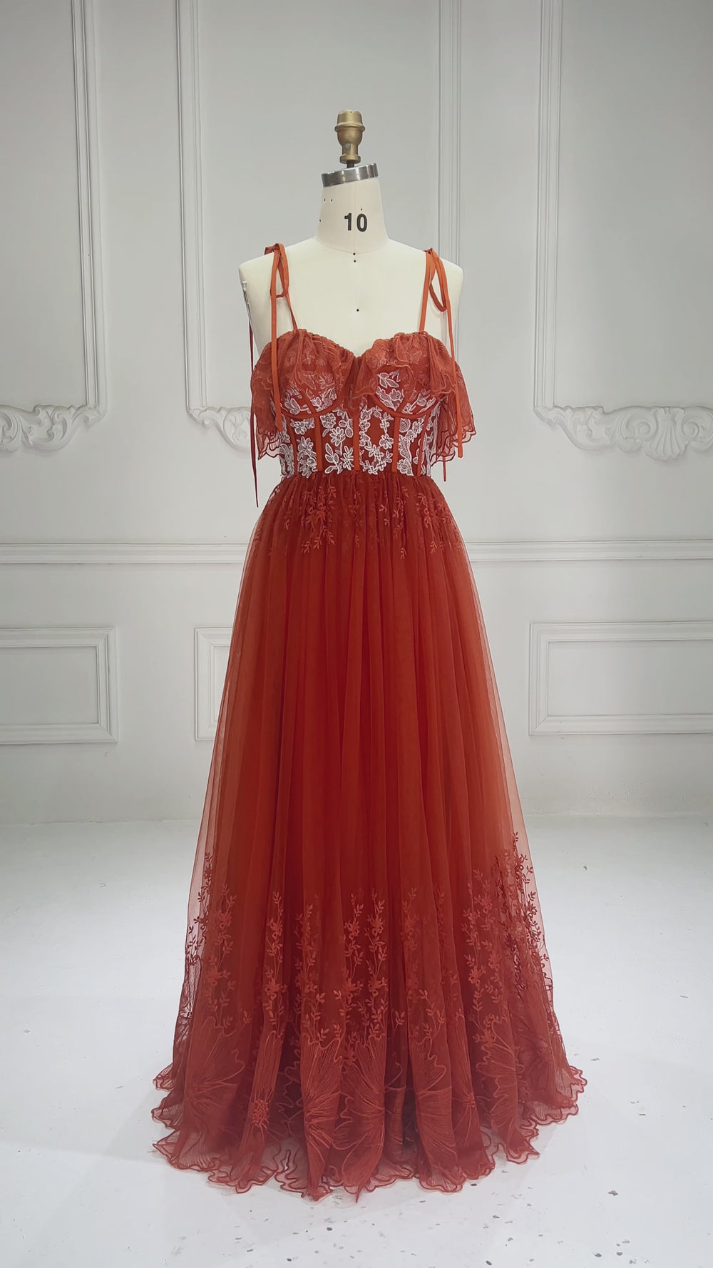 Video showcasing a rust embroidery lace boho photoshoot gown with a strapless sweetheart neckline tie straps a lace-up corset back and a flowing tulle skirt displayed on a mannequin.