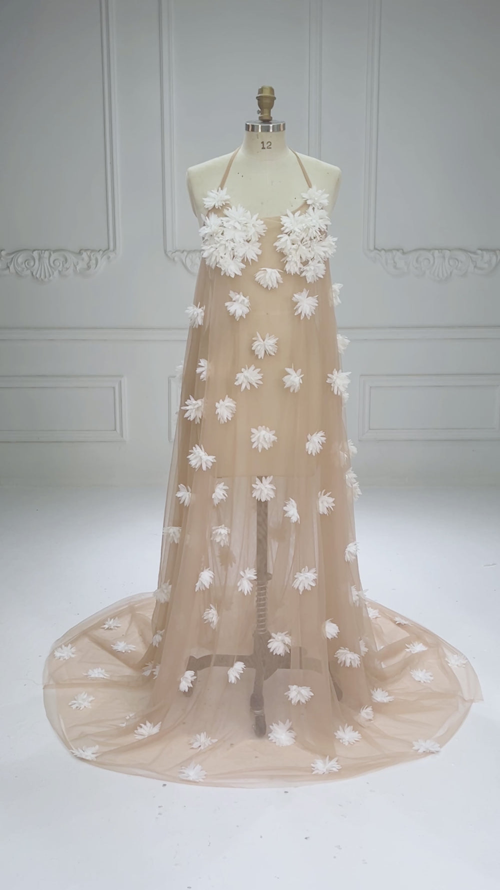 Promotional video showcasing a sheer nude tulle maternity photoshoot dress with 3D white floral appliques and a flowing train displayed on a mannequin.