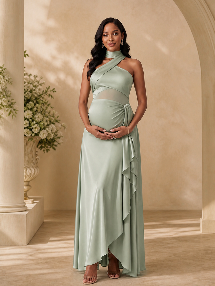 A pregnant model wearing a sage green maternity evening gown with a high-low ruffled hem, standing in a warm, classical stone archway setting.