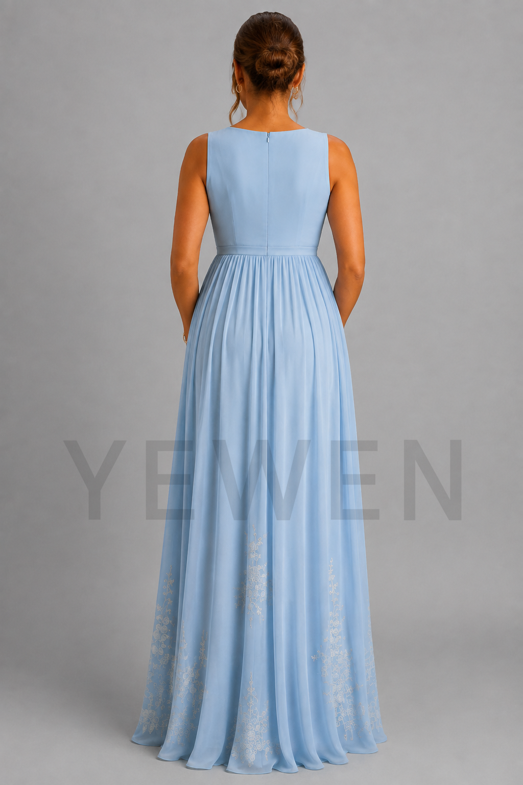 A sleeveless light blue floor-length dress shown from the back on a model against a plain gray studio background. The dress has a structured back and a flowing skirt with subtle tonal lace-like detailing near the lower hem.