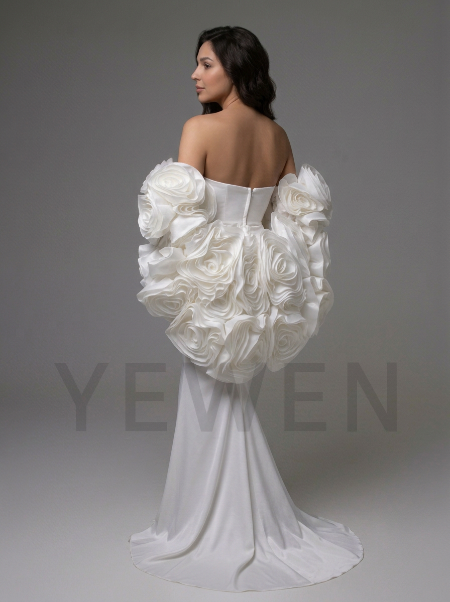 A woman modeling a white off-the-shoulder wedding gown from the back, featuring dramatic sculptural ruffle sleeves and a long train, against a plain gray studio background.