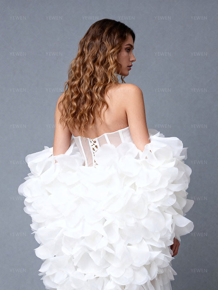 Close-up back view of a model wearing a white 2-piece evening gown highlighting the lace-up corset back and 3D floral cape details.