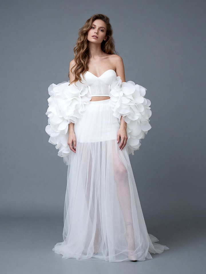 Full front view of a model wearing a white 2-piece evening gown with a 3D floral cape and a sheer tulle skirt.