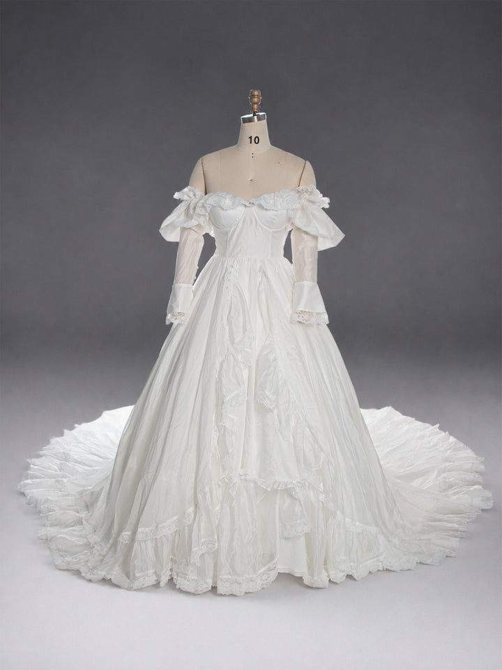 An off-the-shoulder white ball gown with long sheer sleeves and a full tiered skirt, displayed on a dress form against a dark gray studio background.
