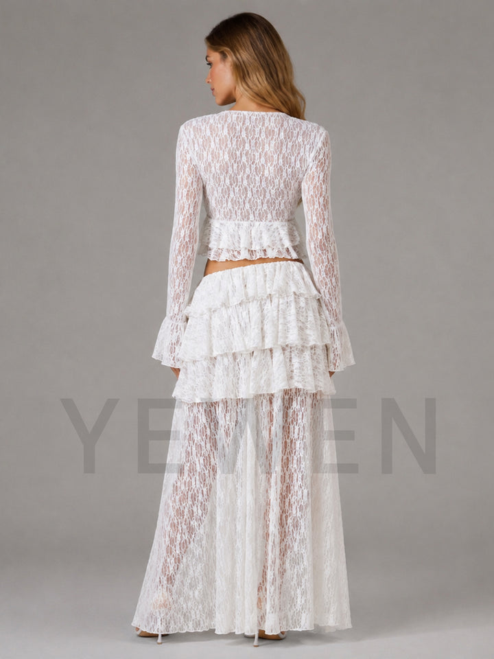 A woman shown from the back wearing a white lace two-piece outfit with a long-sleeve cropped top and a tiered ruffled skirt, photographed against a plain gray studio background.