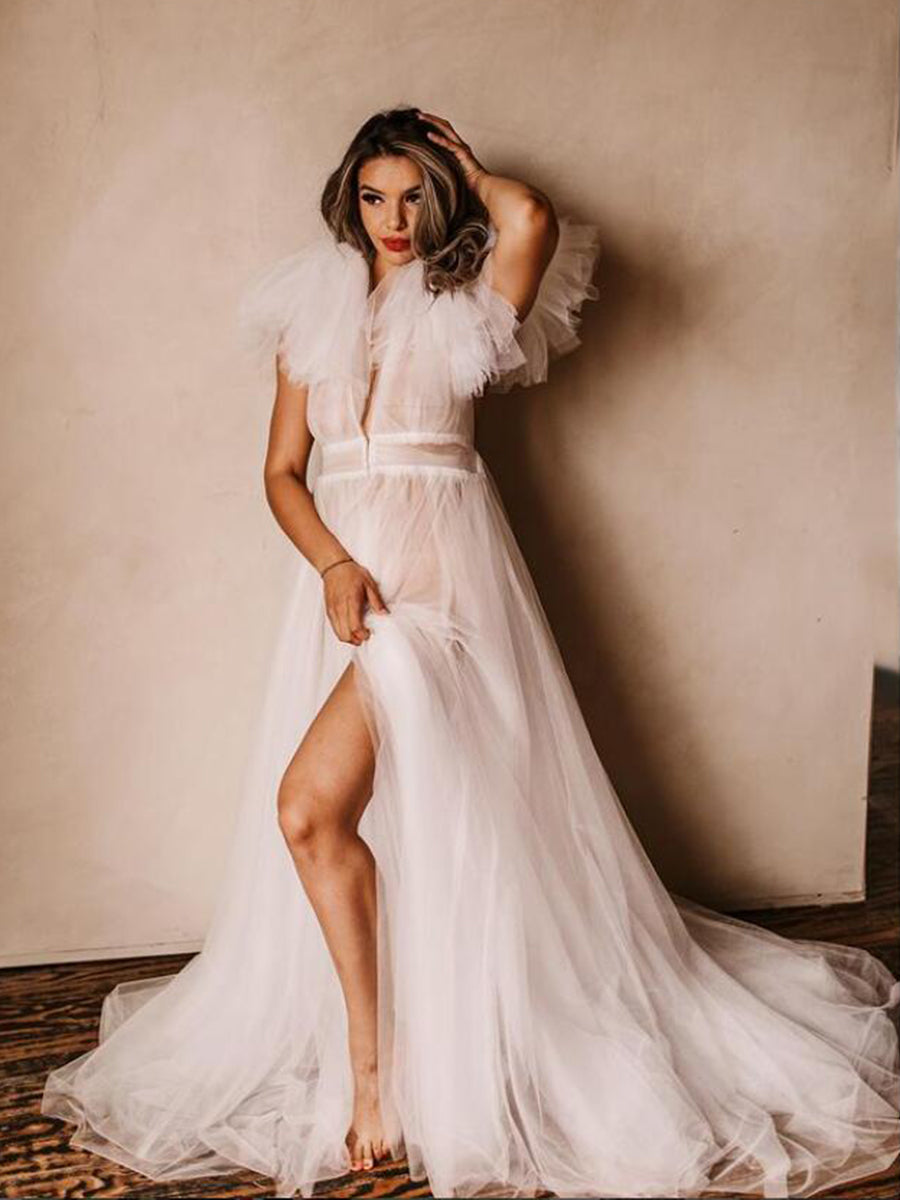 Woman in a white wedding dress with a high slit standing against a plain wall.