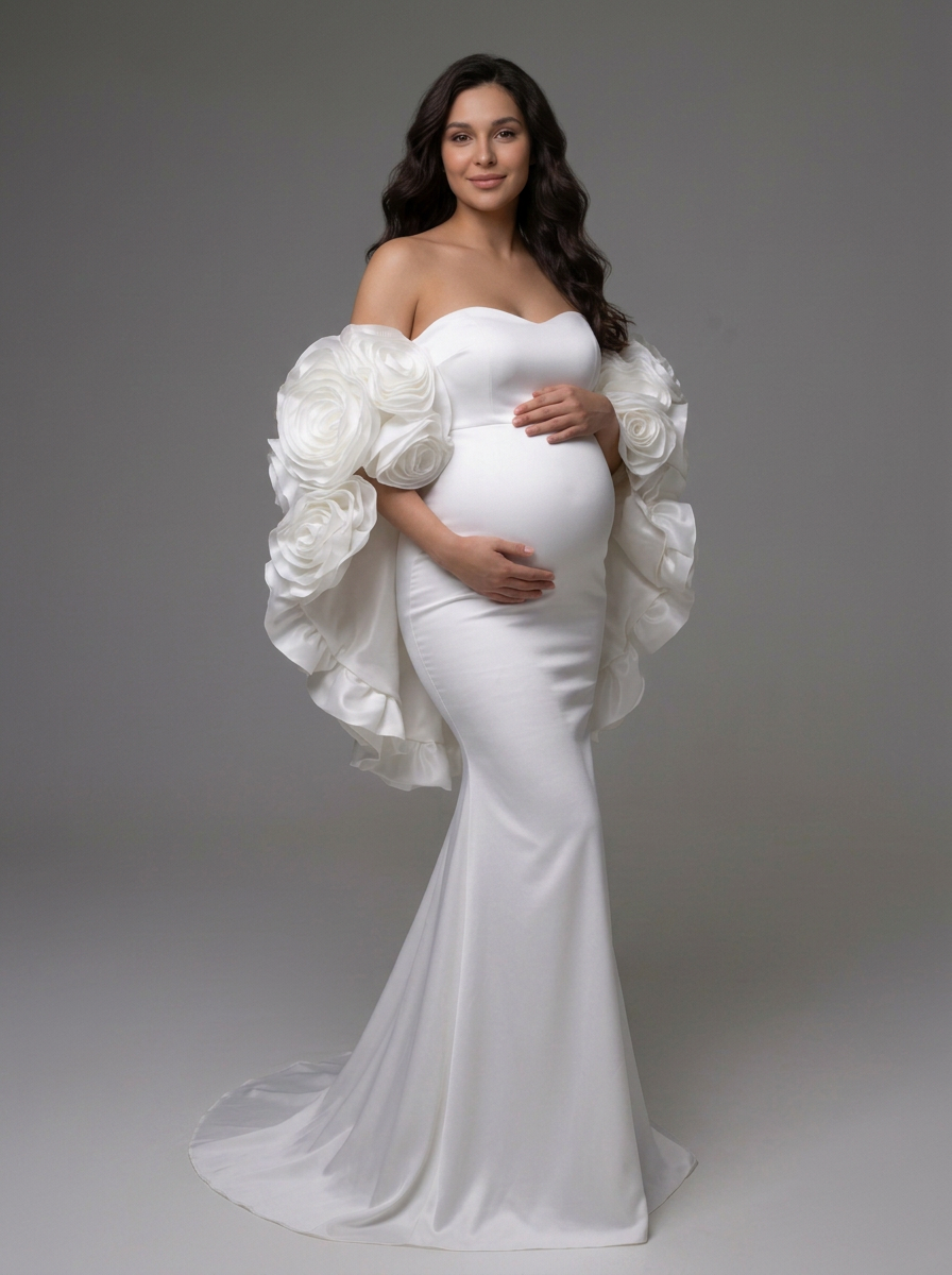 A pregnant model wearing a white strapless mermaid gown with dramatic oversized fabric flower sleeves, photographed against a neutral gray studio background.