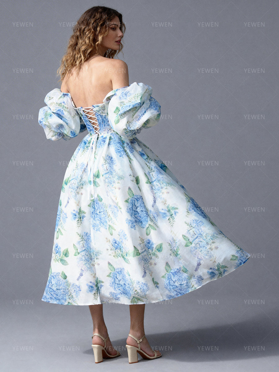Back view of a model wearing a blue floral off-shoulder midi party dress with a fitted bodice and pleated A-line skirt.