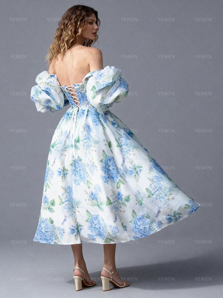 Back view of a model wearing a blue floral off-shoulder midi party dress with a fitted bodice and pleated A-line skirt.