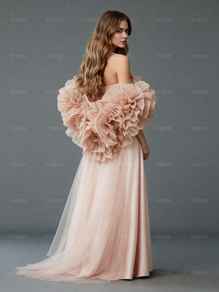 Back view of a model wearing a blush satin prom gown with a 3D ruffle cape and sweeping train.