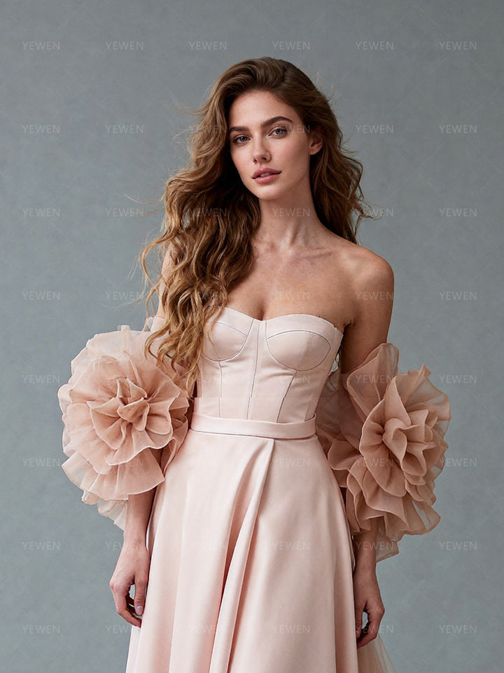 Close-up front view of a model wearing a blush satin prom gown highlighting the corset bodice and 3D ruffle cape details.