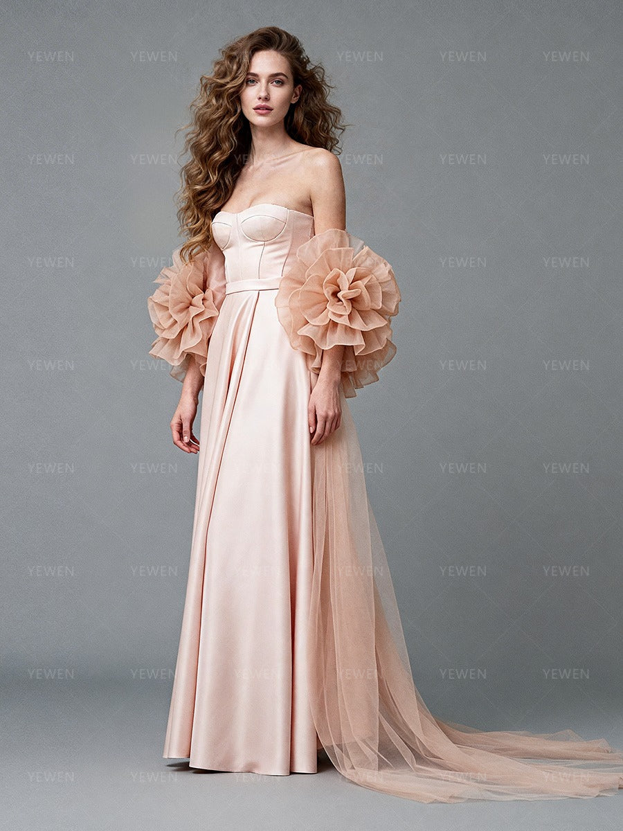 Side view of a model wearing a blush satin prom gown with a 3D ruffle organza cape and flowing skirt.