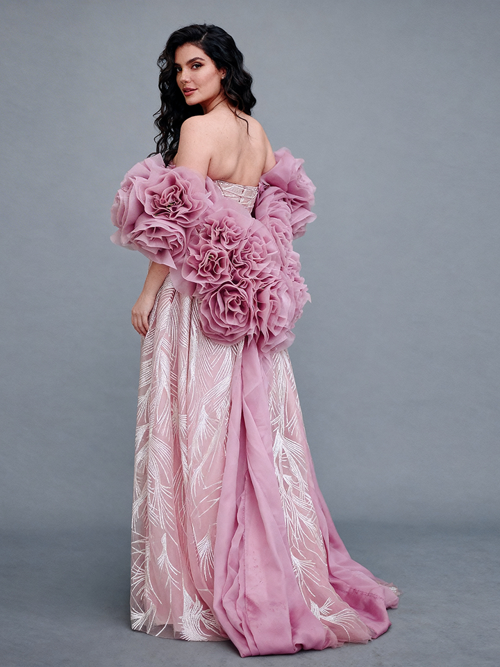 Full back view of a model wearing a blush rose flower cape accessory with oversized floral details and a flowing skirt.