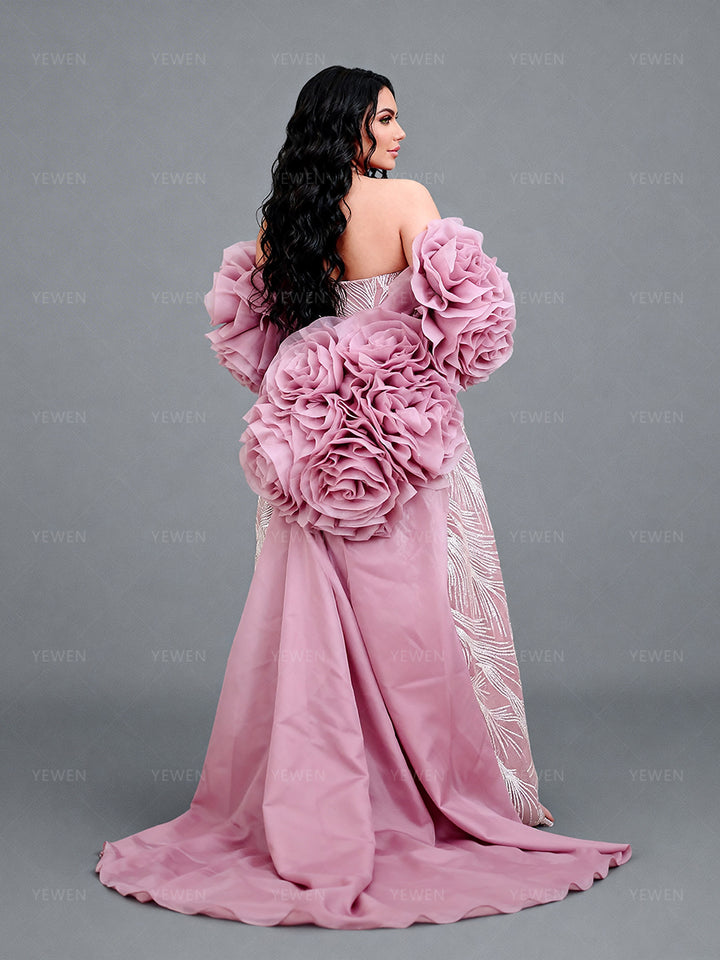 Full back view of a model wearing a blush rose flower cape accessory showing the dramatic floral layers and flowing skirt.