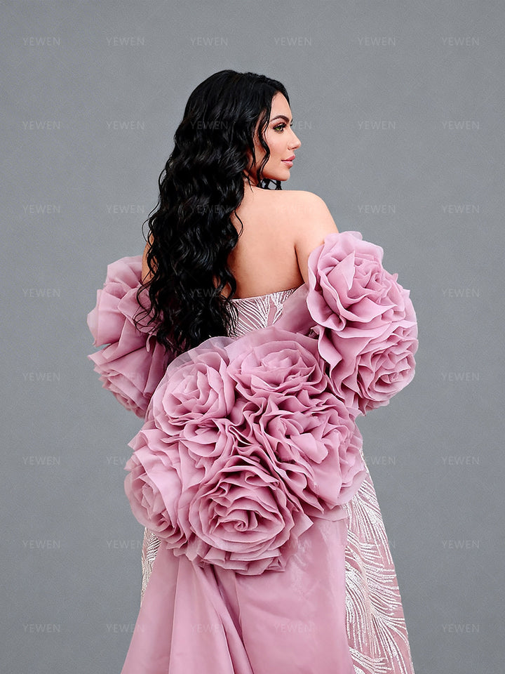 Back side view of a model wearing a blush rose flower cape accessory showcasing the dramatic floral layers and romantic silhouette.